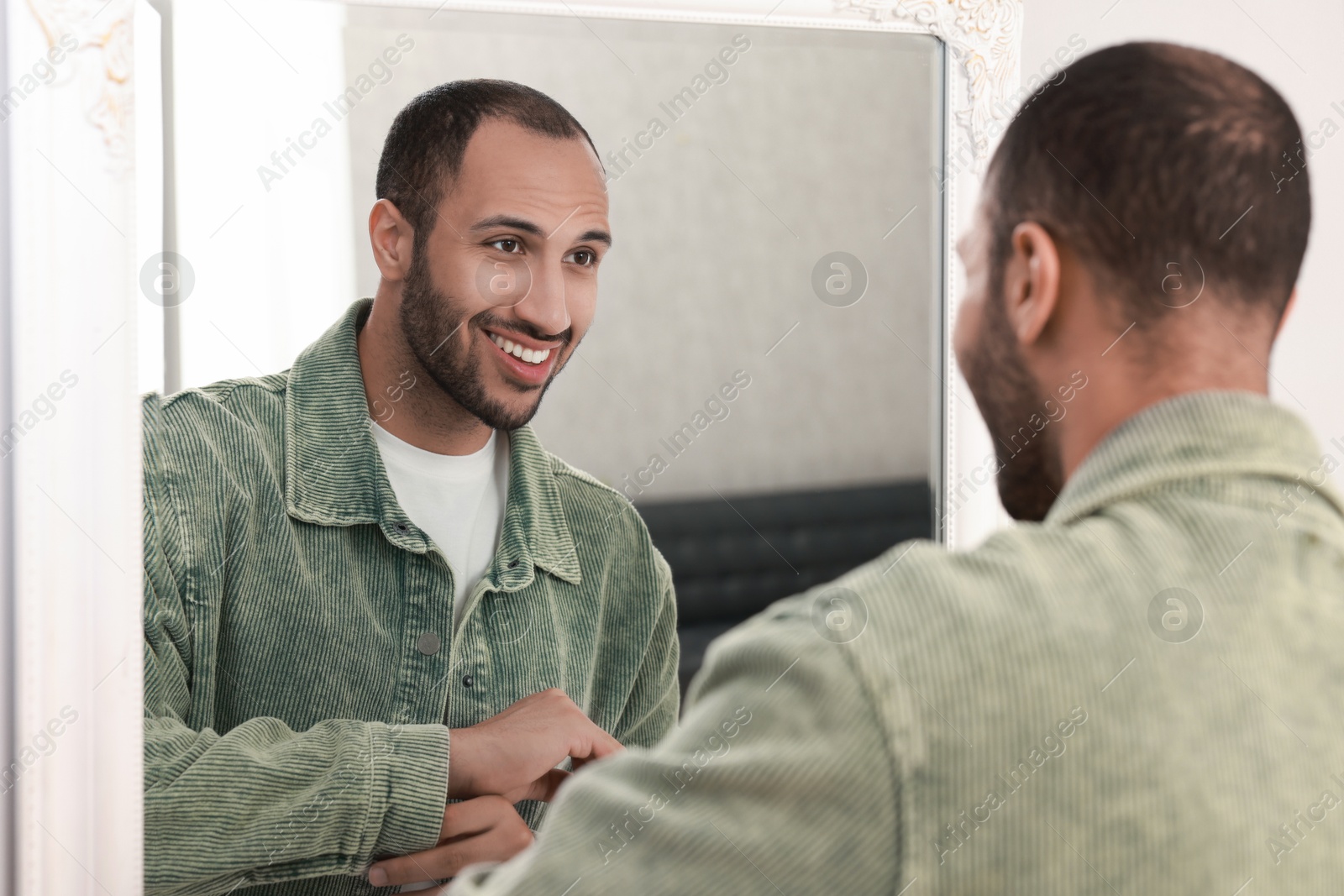 Photo of Smiling man dressing near mirror at home