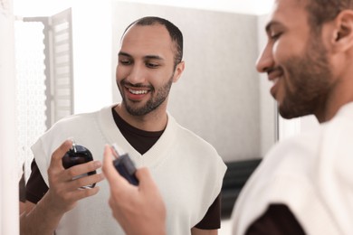 Photo of Smiling man spraying perfume near mirror at home