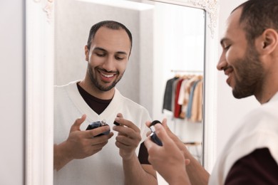 Photo of Smiling man spraying perfume near mirror at home