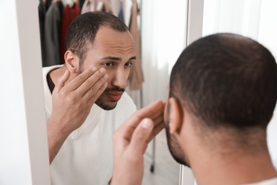 Photo of Worried man looking at mirror at home