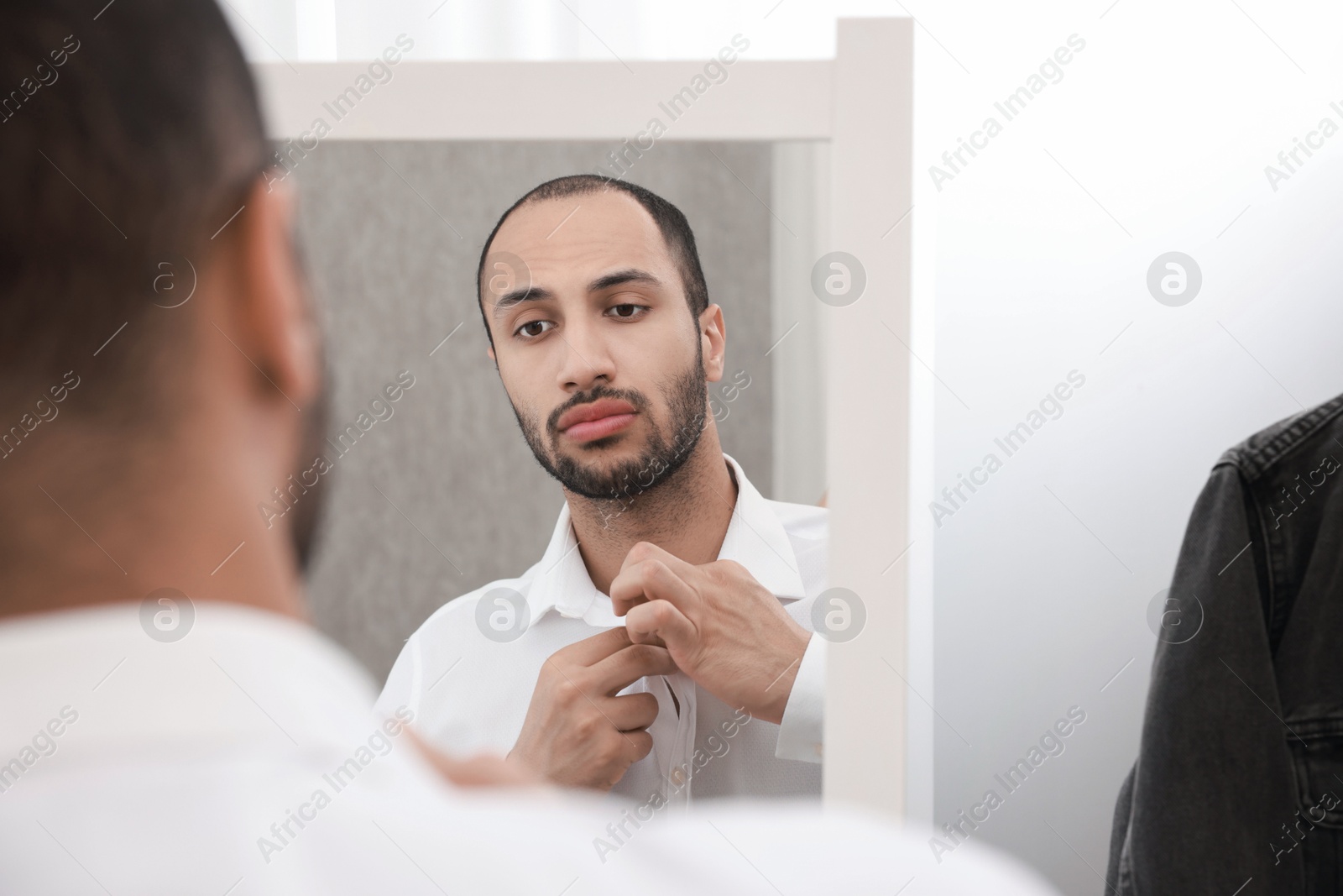 Photo of Handsome man dressing near mirror at home