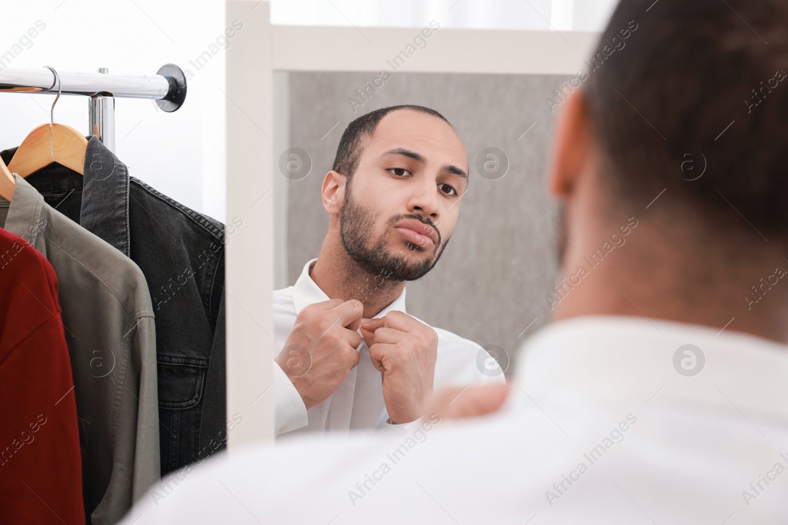 Photo of Handsome man dressing near mirror at home