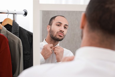 Photo of Handsome man dressing near mirror at home