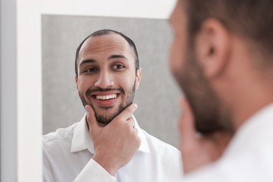 Photo of Smiling man looking at mirror at home