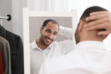 Photo of Smiling man looking at mirror at home, back view