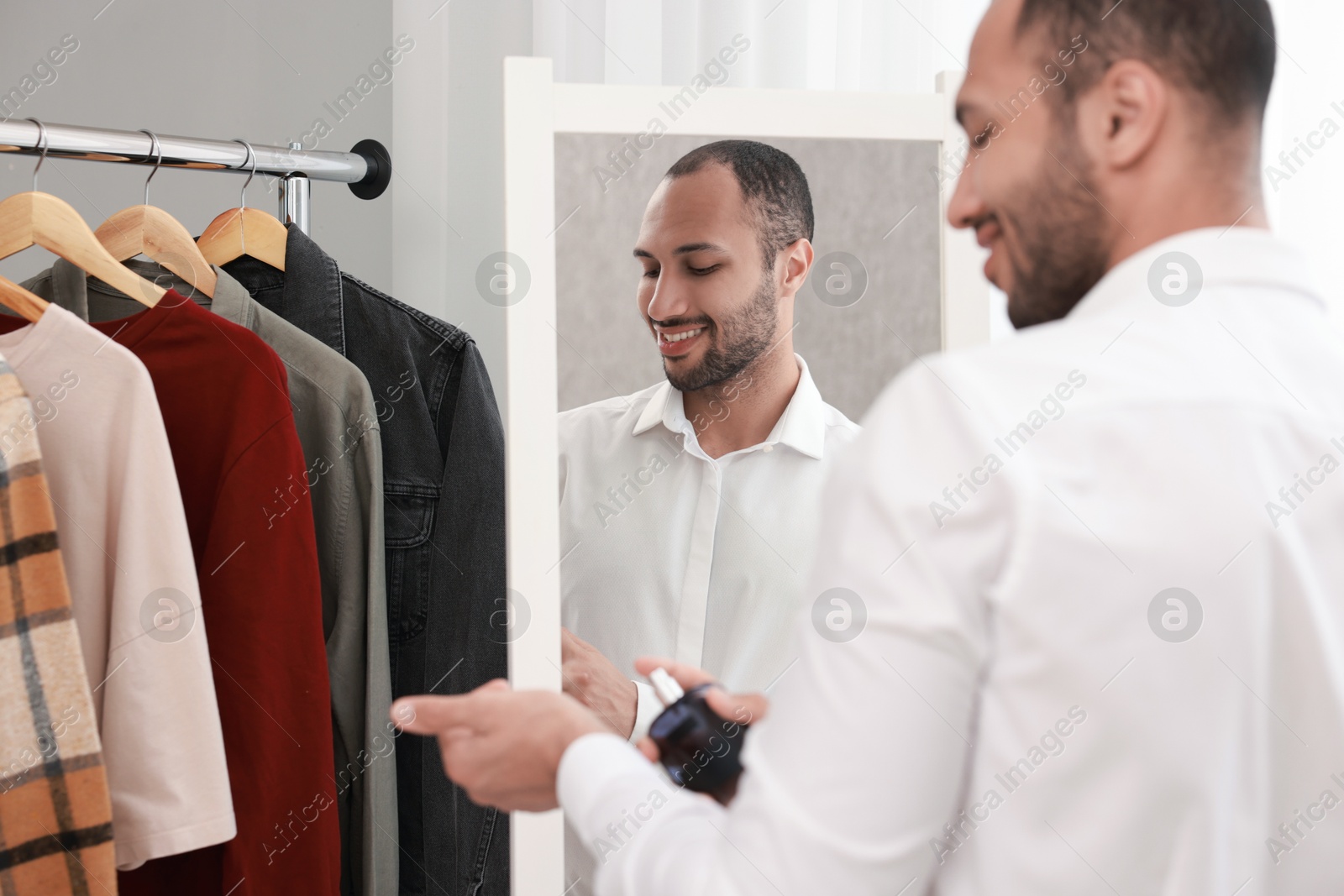 Photo of Smiling man spraying perfume near mirror at home, back view