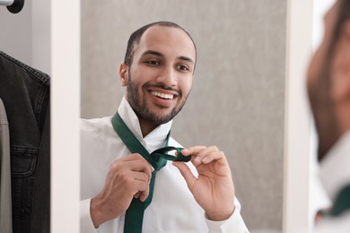 Photo of Smiling man adjusting necktie near mirror at home