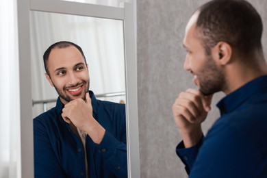 Photo of Smiling man looking at mirror at home