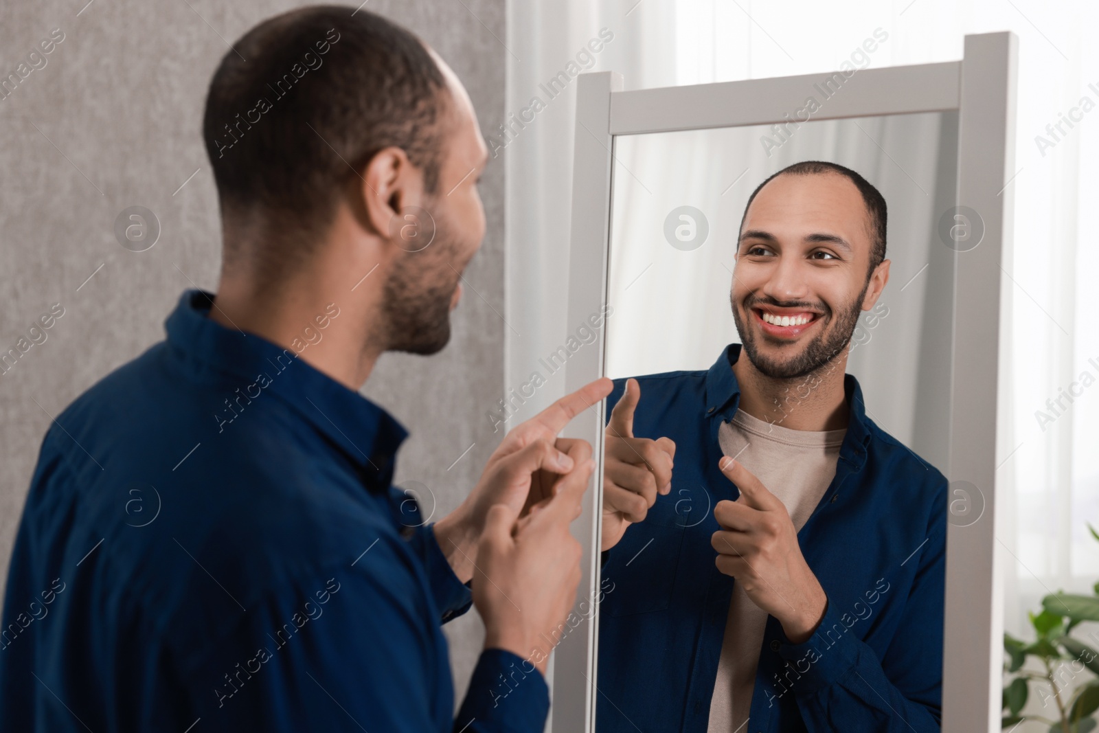 Photo of Smiling man looking at mirror at home