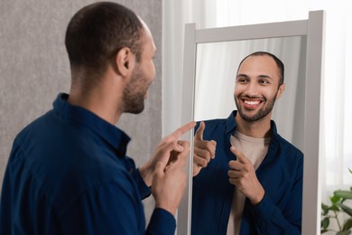 Smiling man looking at mirror at home