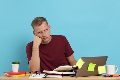 Photo of Preparing for exam. Student with laptop and books at table against light blue background