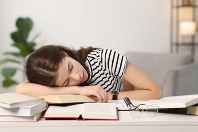 Photo of Preparing for exam. Tired student sleeping among books at table indoors