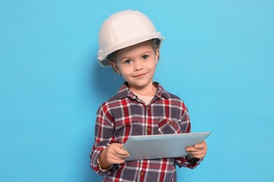 Photo of Little girl with tablet pretending to be architect on light blue background. Dreaming of future profession