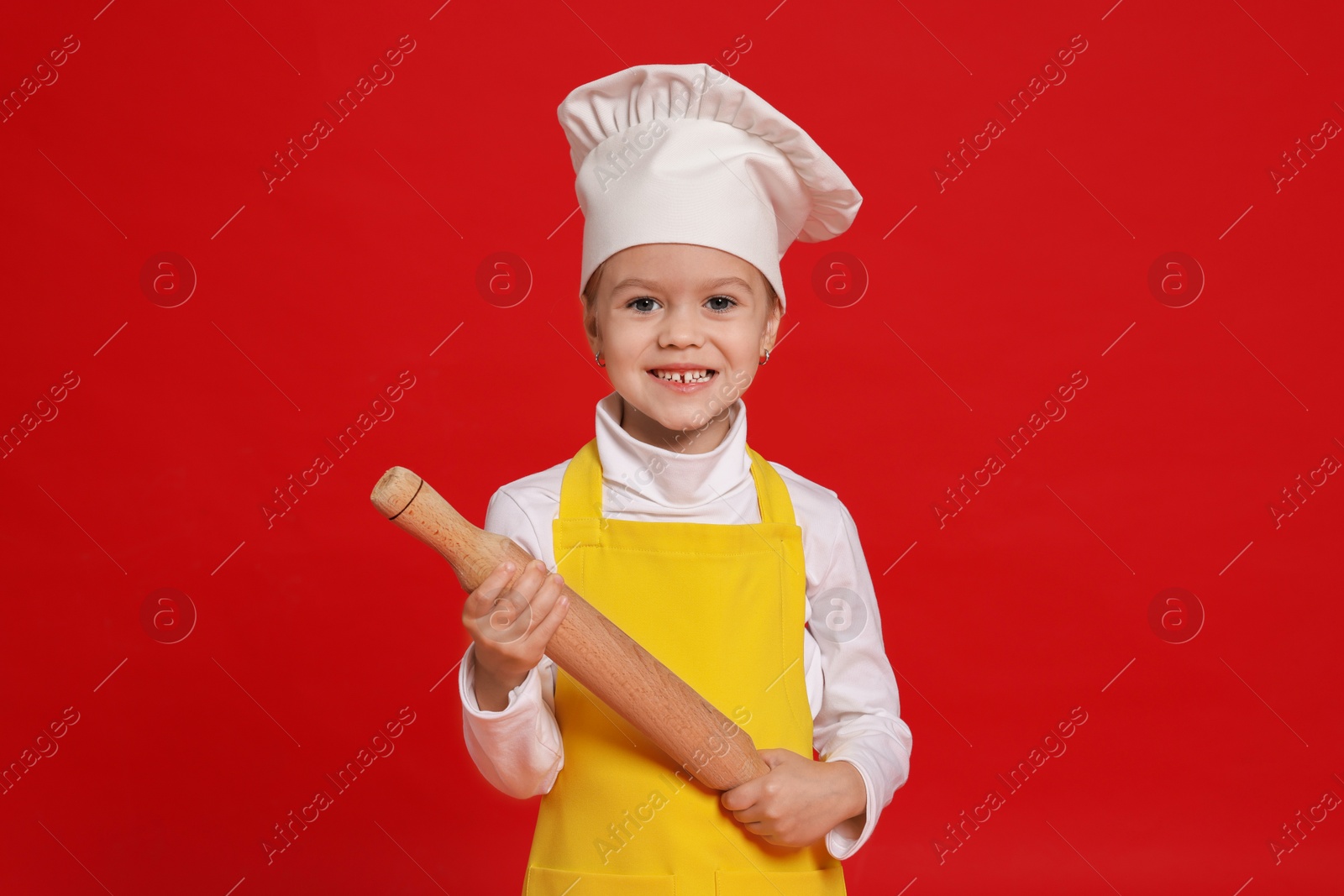 Photo of Little girl with rolling pin pretending to be chef on red background. Dreaming of future profession