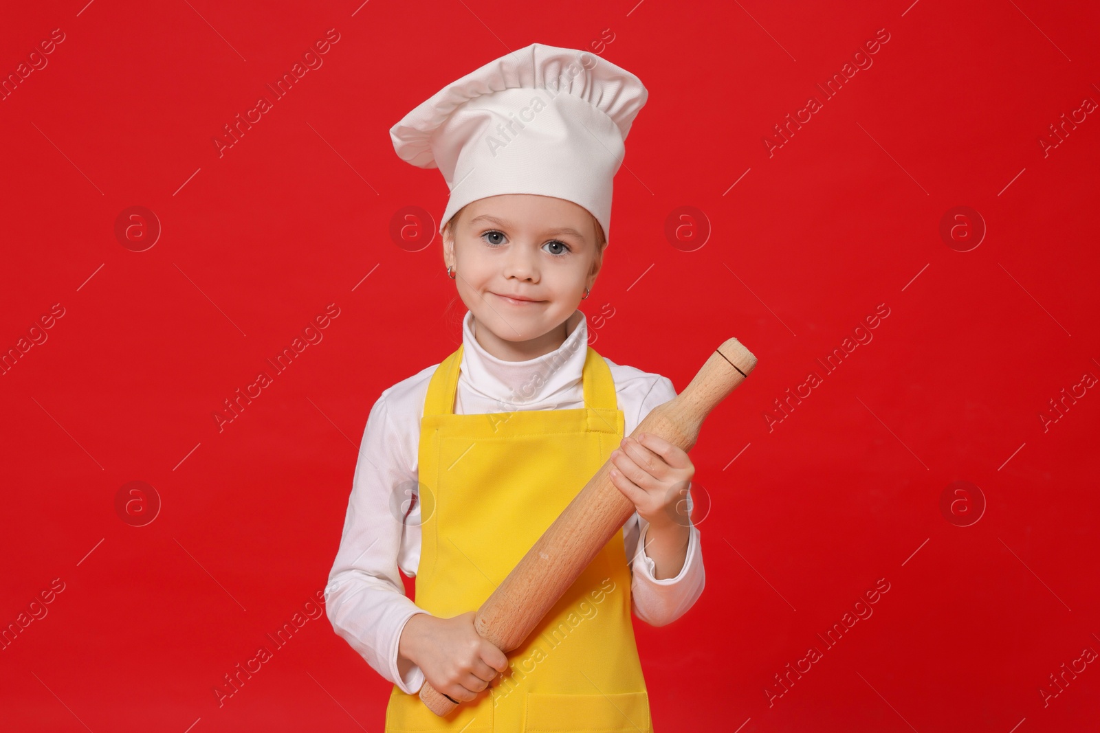 Photo of Little girl with rolling pin pretending to be chef on red background. Dreaming of future profession