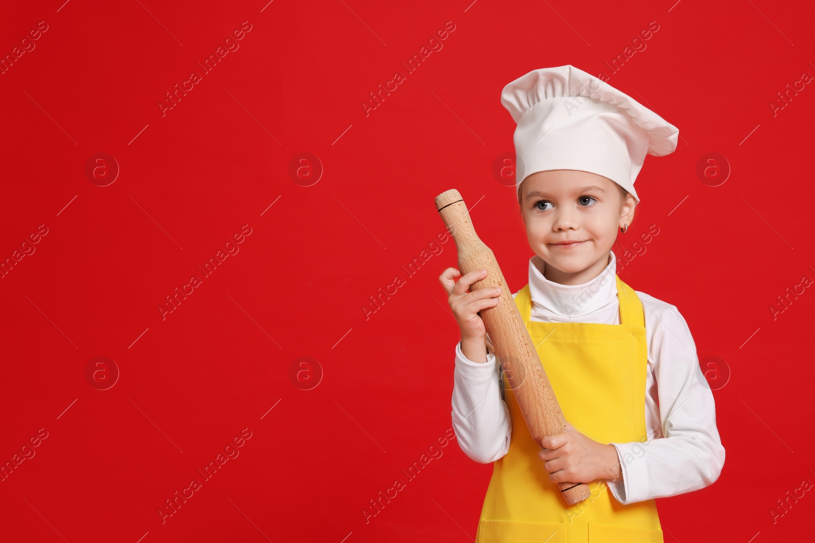 Photo of Little girl with rolling pin pretending to be chef on red background, space for text. Dreaming of future profession