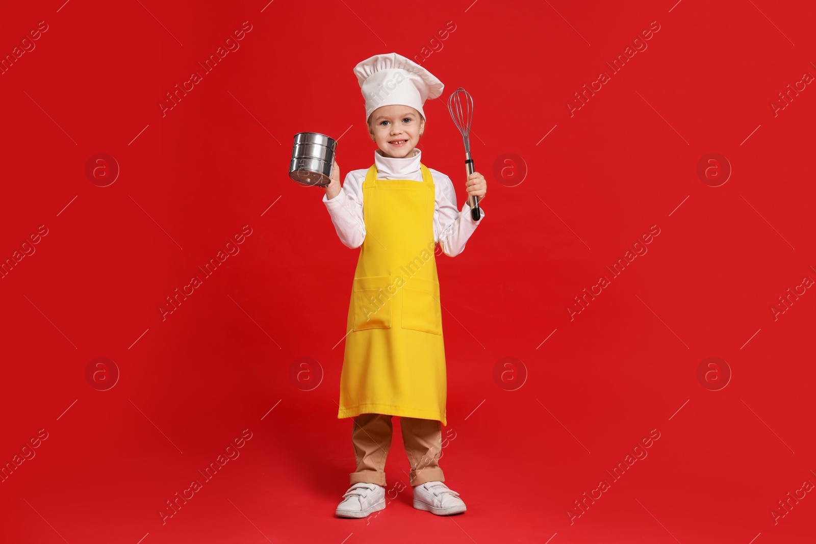 Photo of Little girl with utensils pretending to be chef on red background. Dreaming of future profession