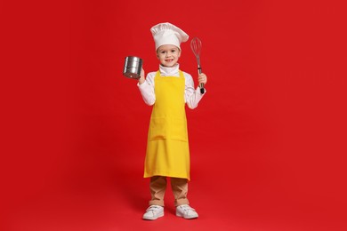 Photo of Little girl with utensils pretending to be chef on red background. Dreaming of future profession