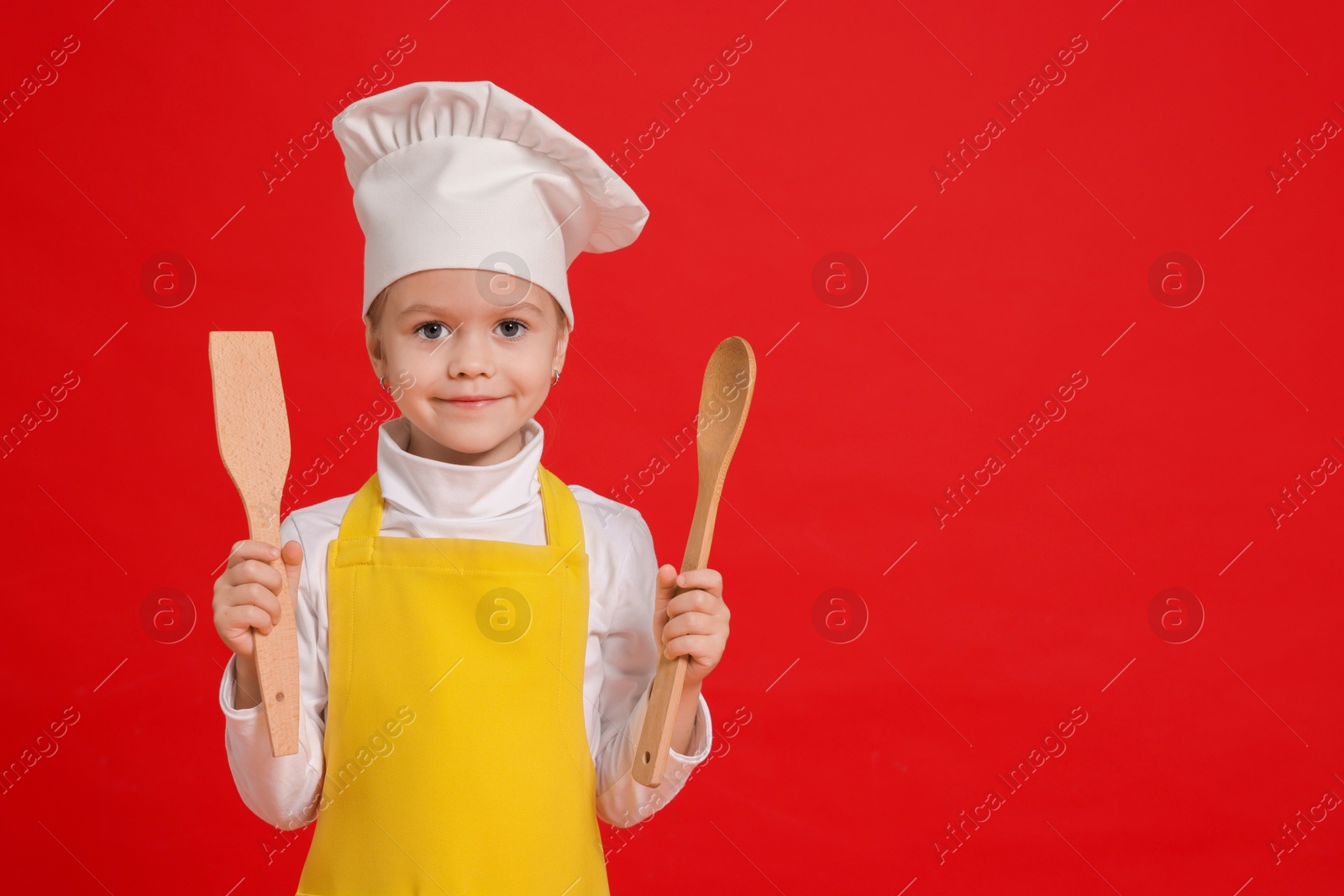 Photo of Little girl with utensils pretending to be chef on red background, space for text. Dreaming of future profession