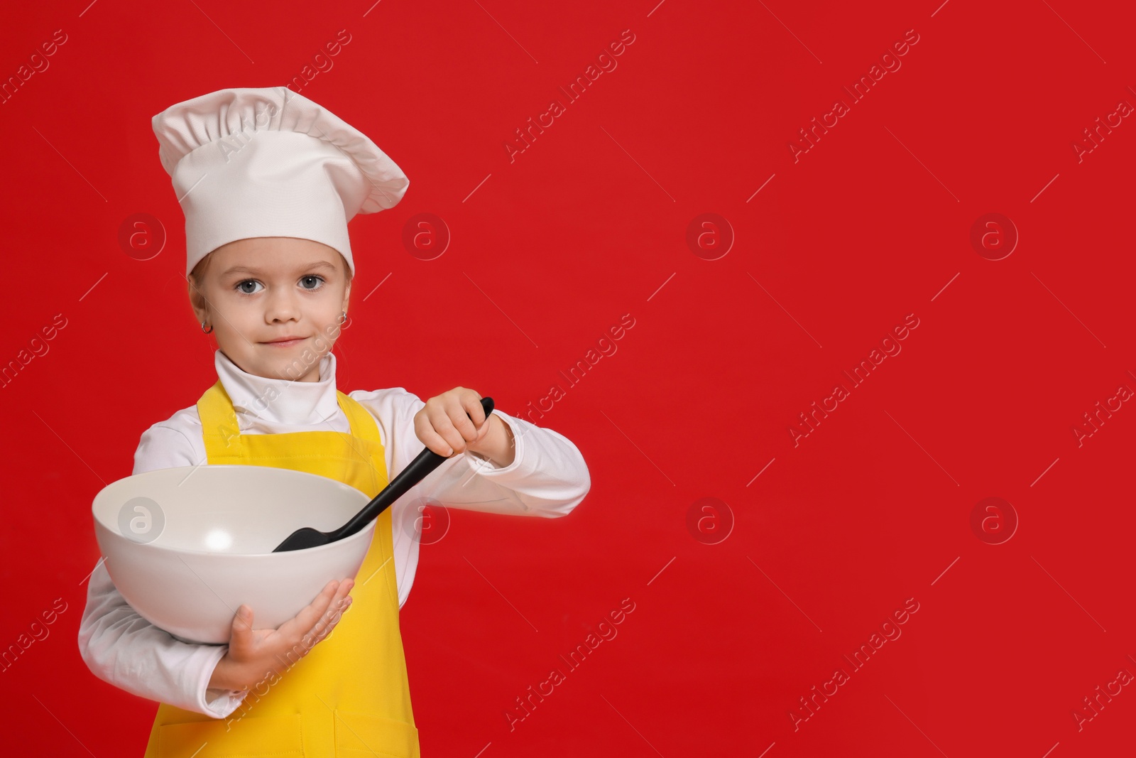 Photo of Little girl with bowl and spoon pretending to be chef on red background, space for text. Dreaming of future profession