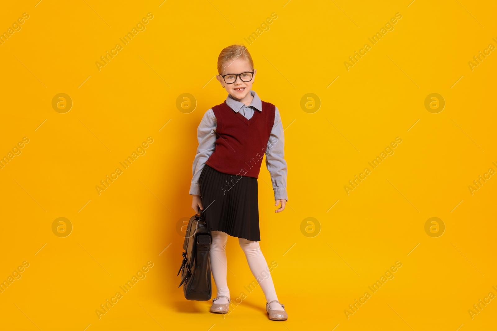 Photo of Little girl with glasses and briefcase on orange background. Dreaming of future profession