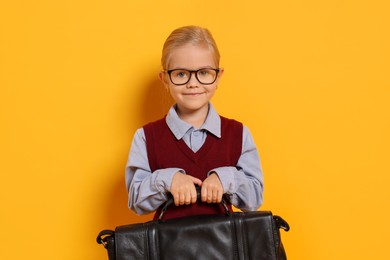 Photo of Little girl with glasses and briefcase on orange background. Dreaming of future profession