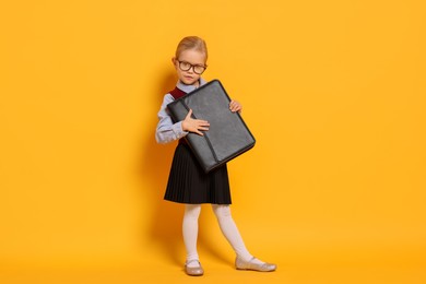 Photo of Little girl with glasses and briefcase on orange background. Dreaming of future profession