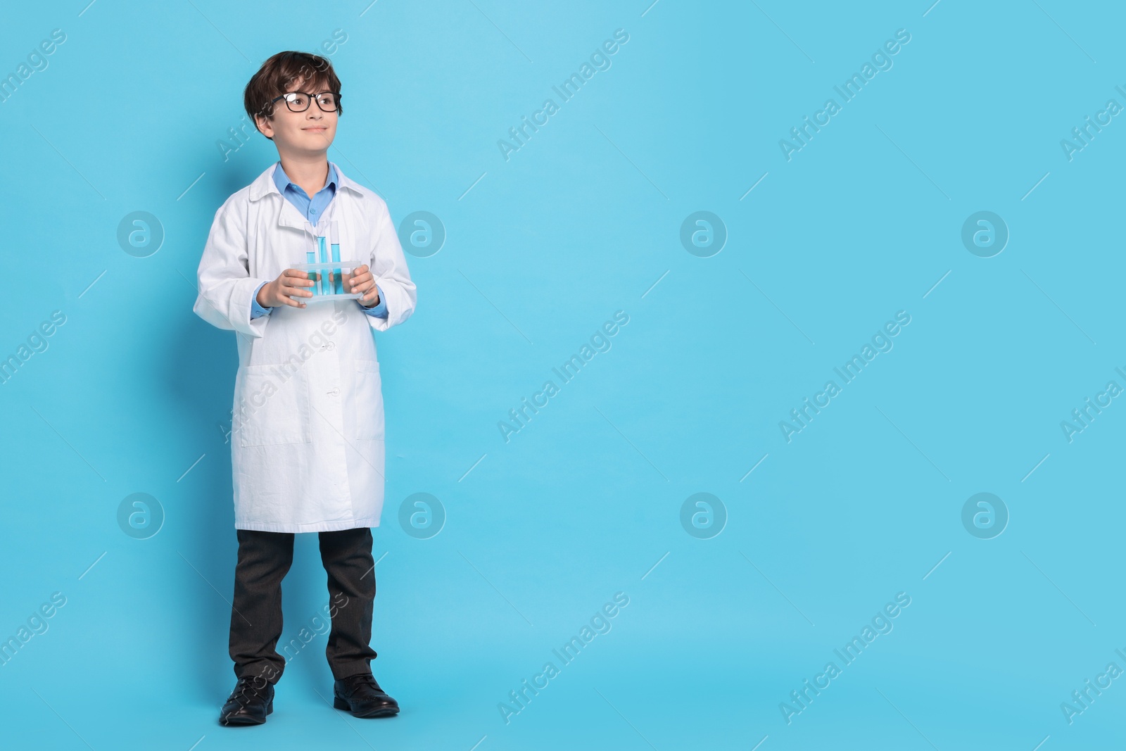 Photo of Boy with test tubes pretending to be scientist on light blue background, space for text. Dreaming of future profession