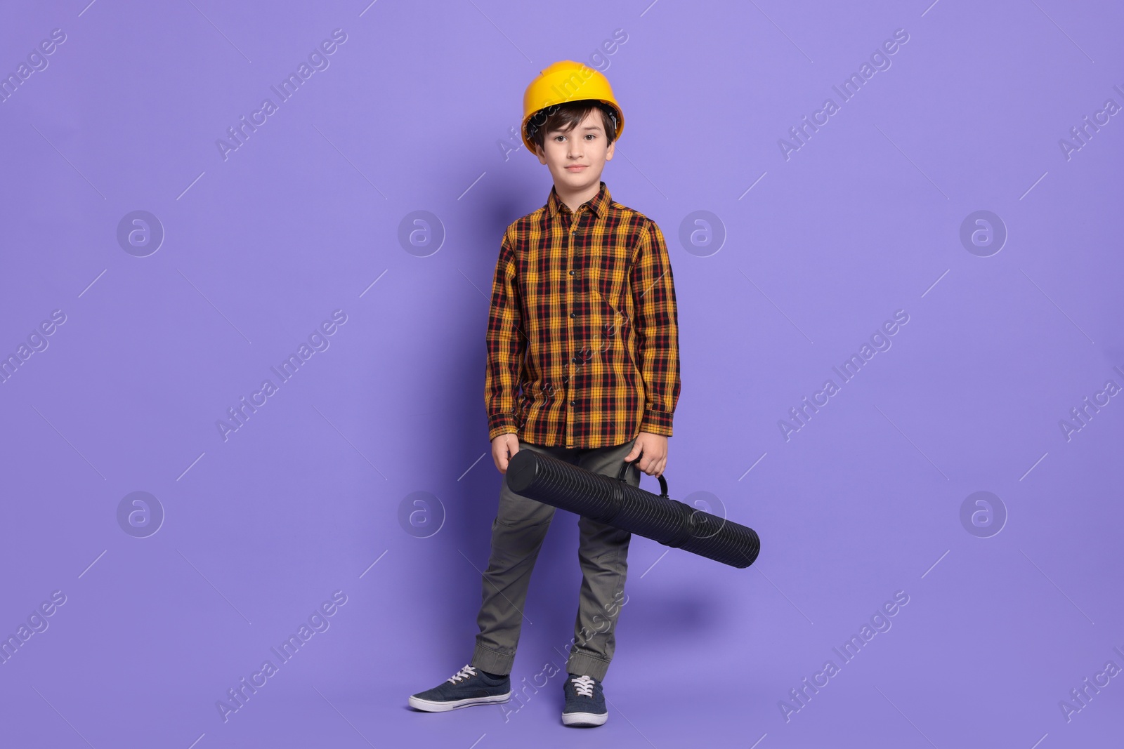 Photo of Boy with blueprint tube pretending to be architect on violet background. Dreaming of future profession