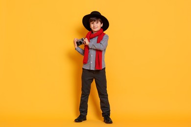 Photo of Boy with camera pretending to be photographer on orange background. Dreaming of future profession