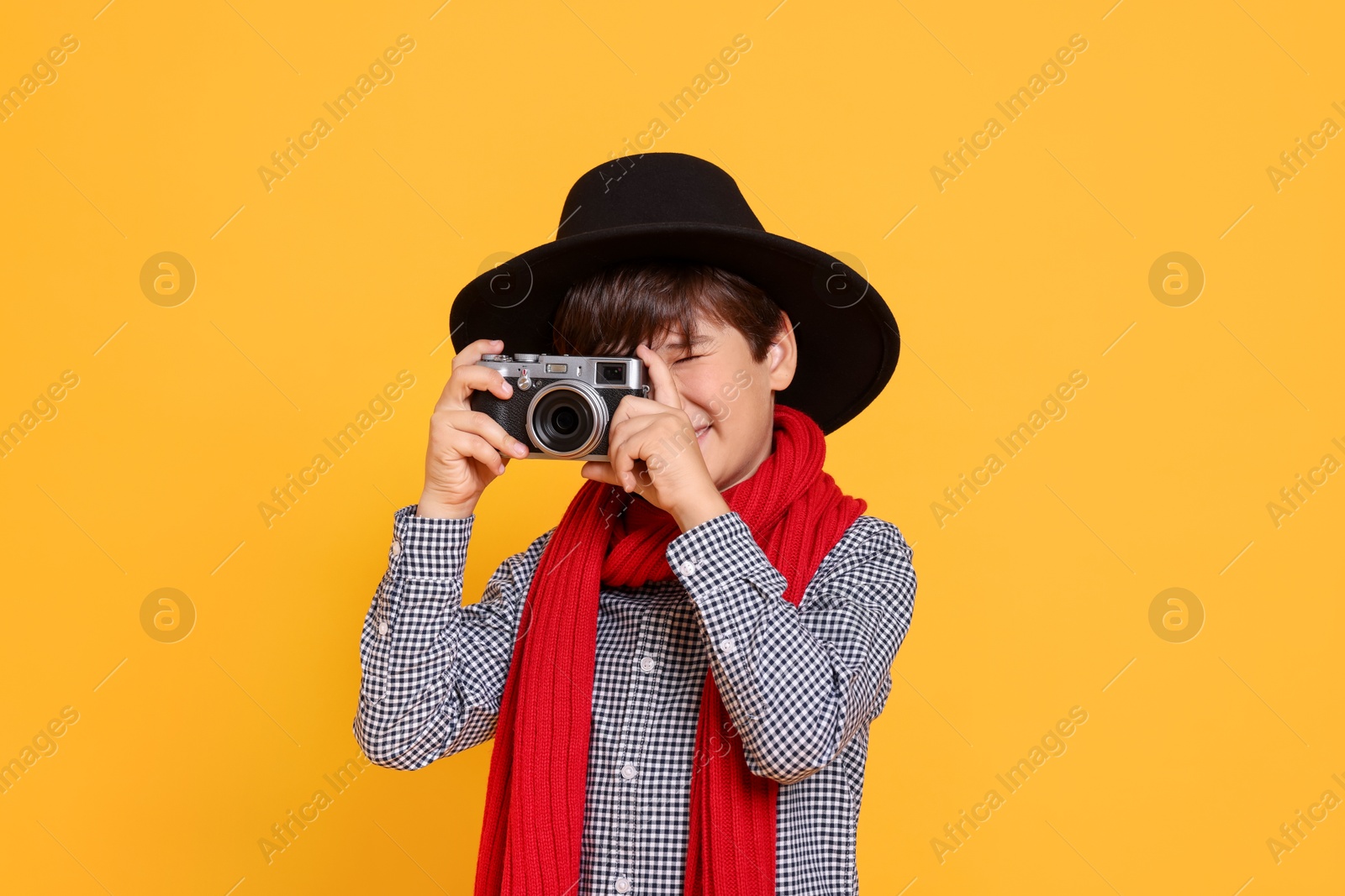 Photo of Boy with camera pretending to be photographer on orange background. Dreaming of future profession