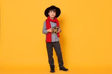 Photo of Boy with film reel pretending to be movie director on orange background. Dreaming of future profession