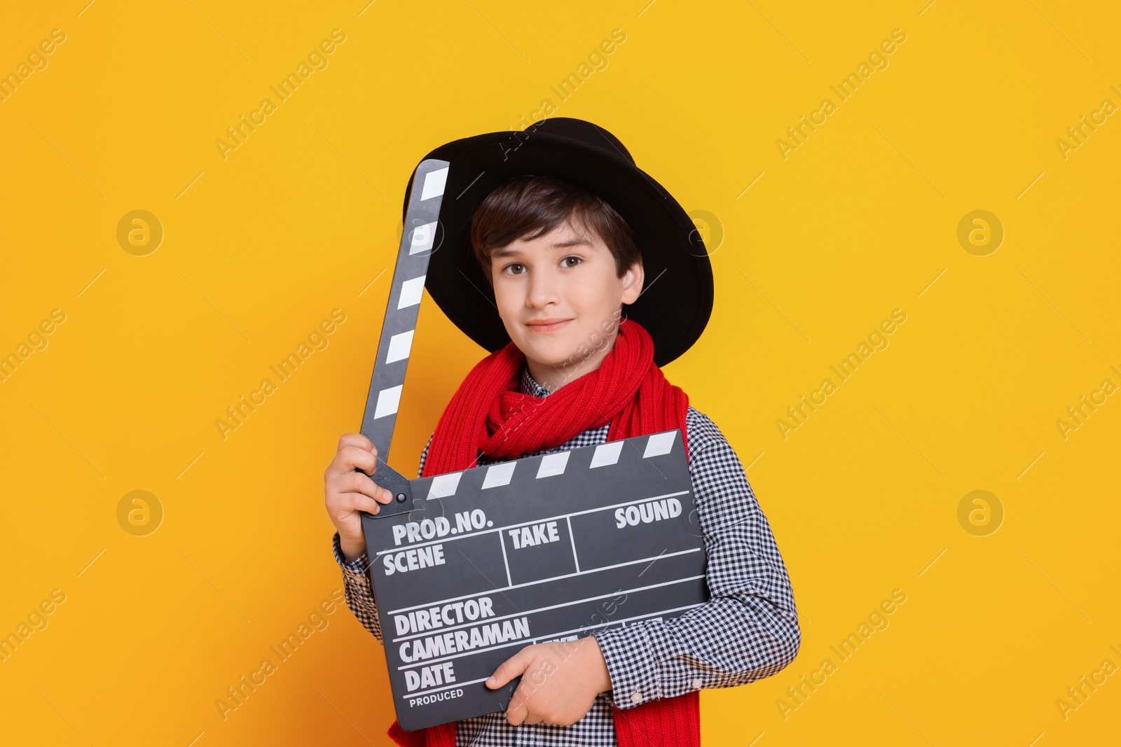 Photo of Boy with clapper pretending to be movie director on orange background. Dreaming of future profession