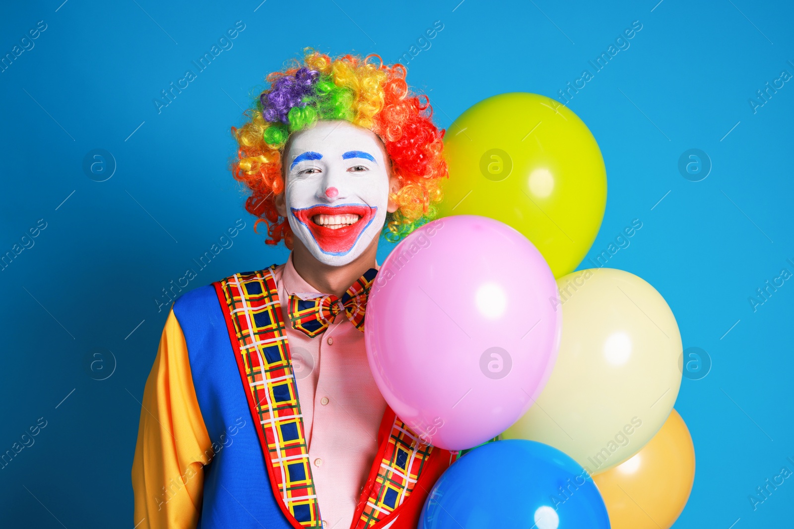 Photo of Happy clown with colorful balloons on blue background