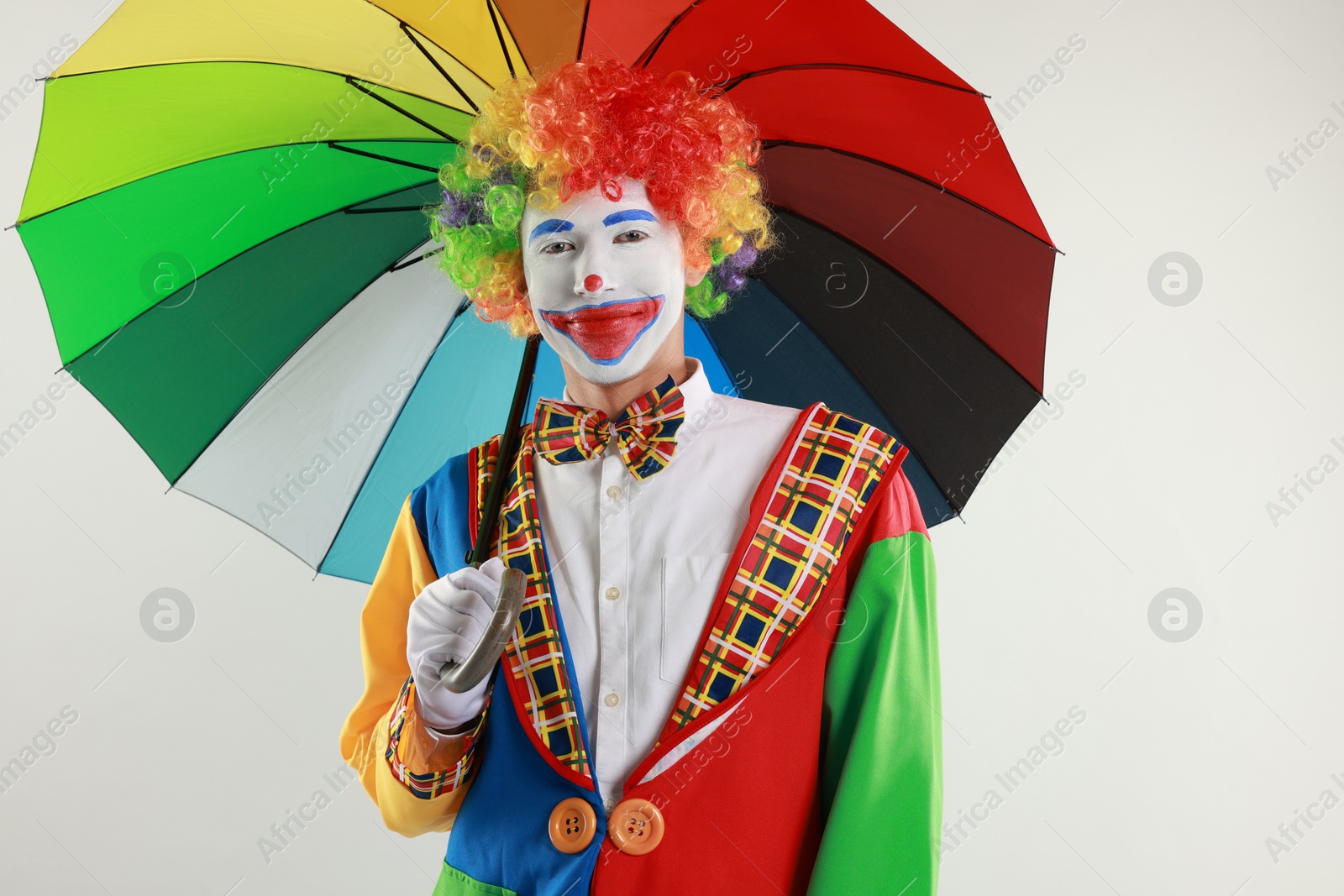 Photo of Clown with colorful umbrella on light background