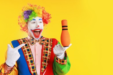 Photo of Emotional clown with juggling club on yellow background, space for text