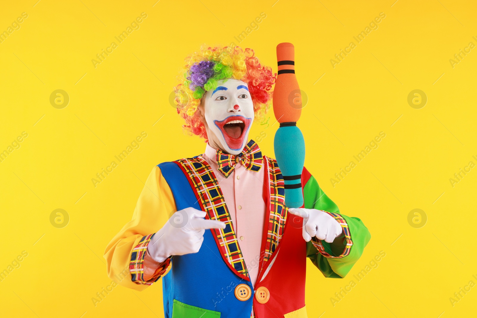 Photo of Emotional clown with juggling clubs on yellow background