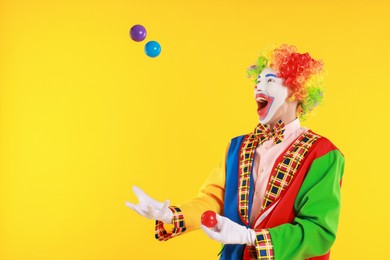 Photo of Emotional clown juggling balls on yellow background, space for text