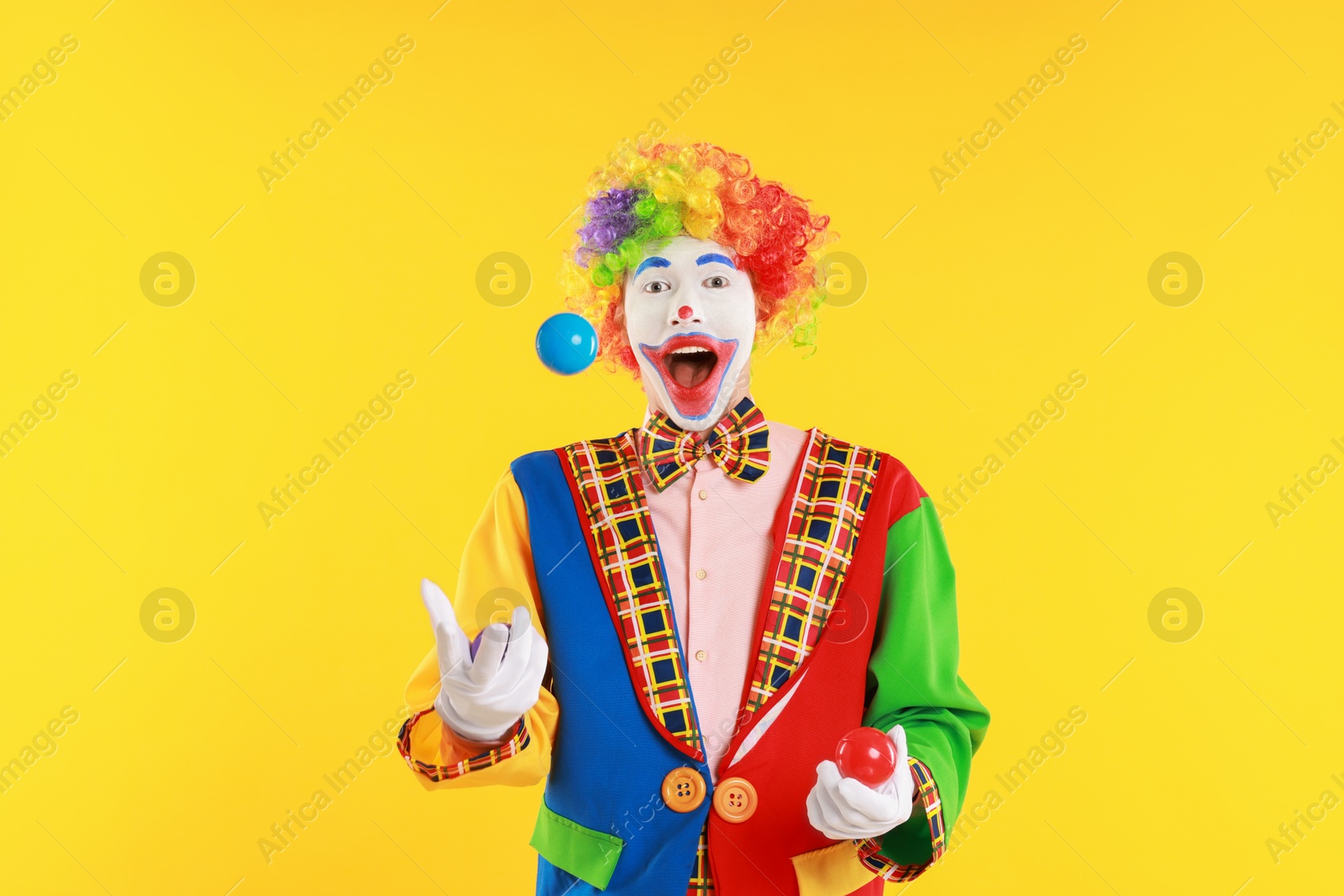 Photo of Emotional clown juggling balls on yellow background