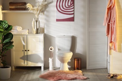 Photo of Ceramic toilet bowl, folding screen and necessities in restroom