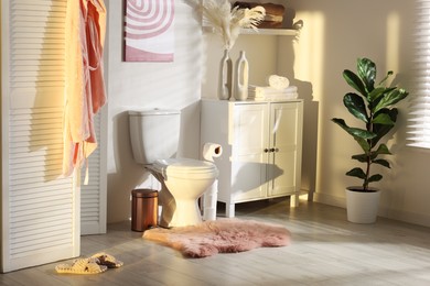 Photo of Ceramic toilet bowl, folding screen and necessities in restroom