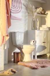 Photo of Ceramic toilet bowl, folding screen and necessities in restroom