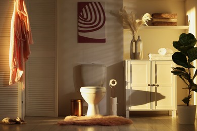 Photo of Ceramic toilet bowl, folding screen and necessities in restroom