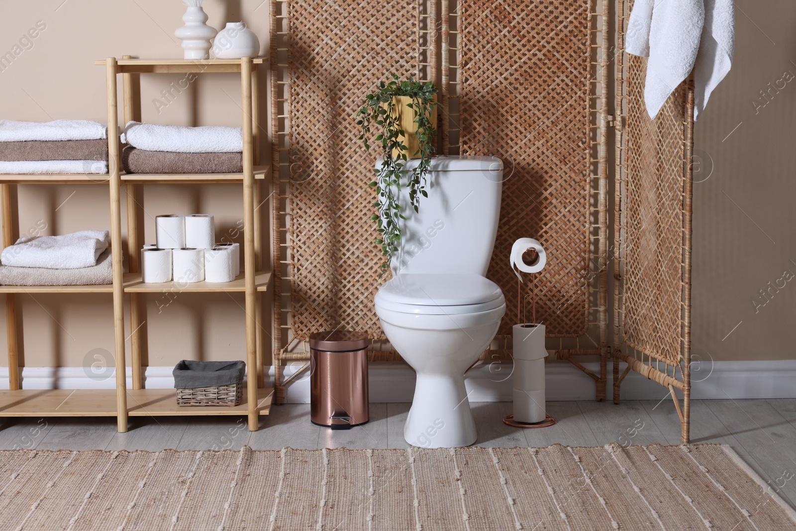 Photo of Ceramic toilet bowl, folding screen and necessities in restroom