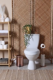 Photo of Ceramic toilet bowl, folding screen and necessities in restroom