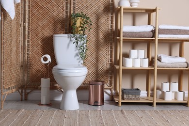 Photo of Ceramic toilet bowl, folding screen and necessities in restroom