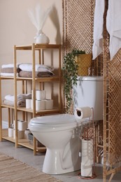 Photo of Ceramic toilet bowl, folding screen and necessities in restroom