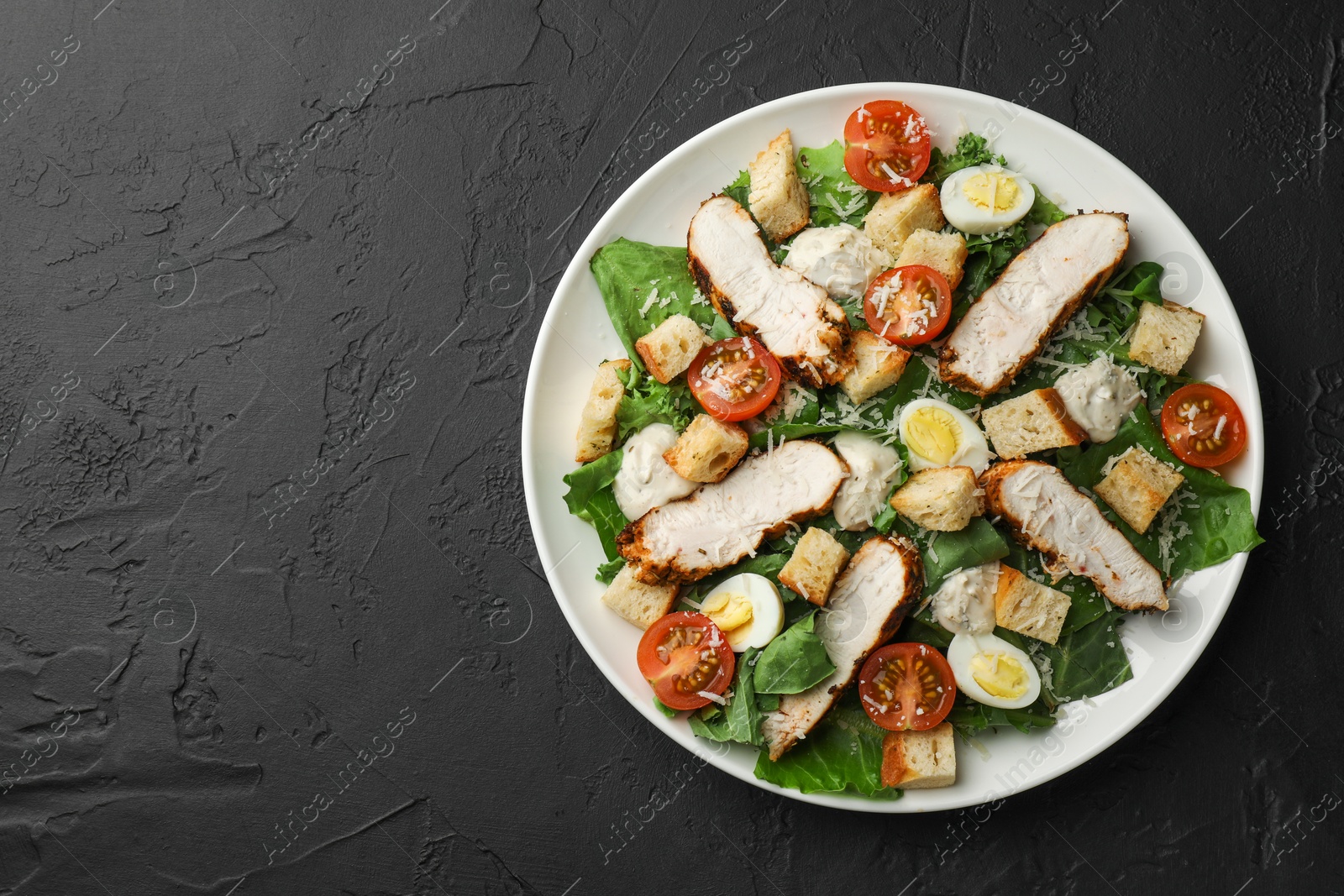 Photo of Tasty Caesar salad with chicken and tomatoes on black table, top view. Space for text