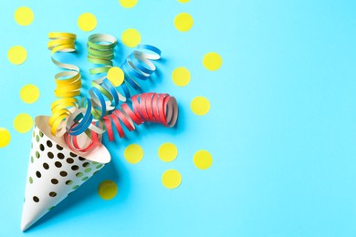 Photo of Party hat with confetti and streamers on light blue background, flat lay. Space for text