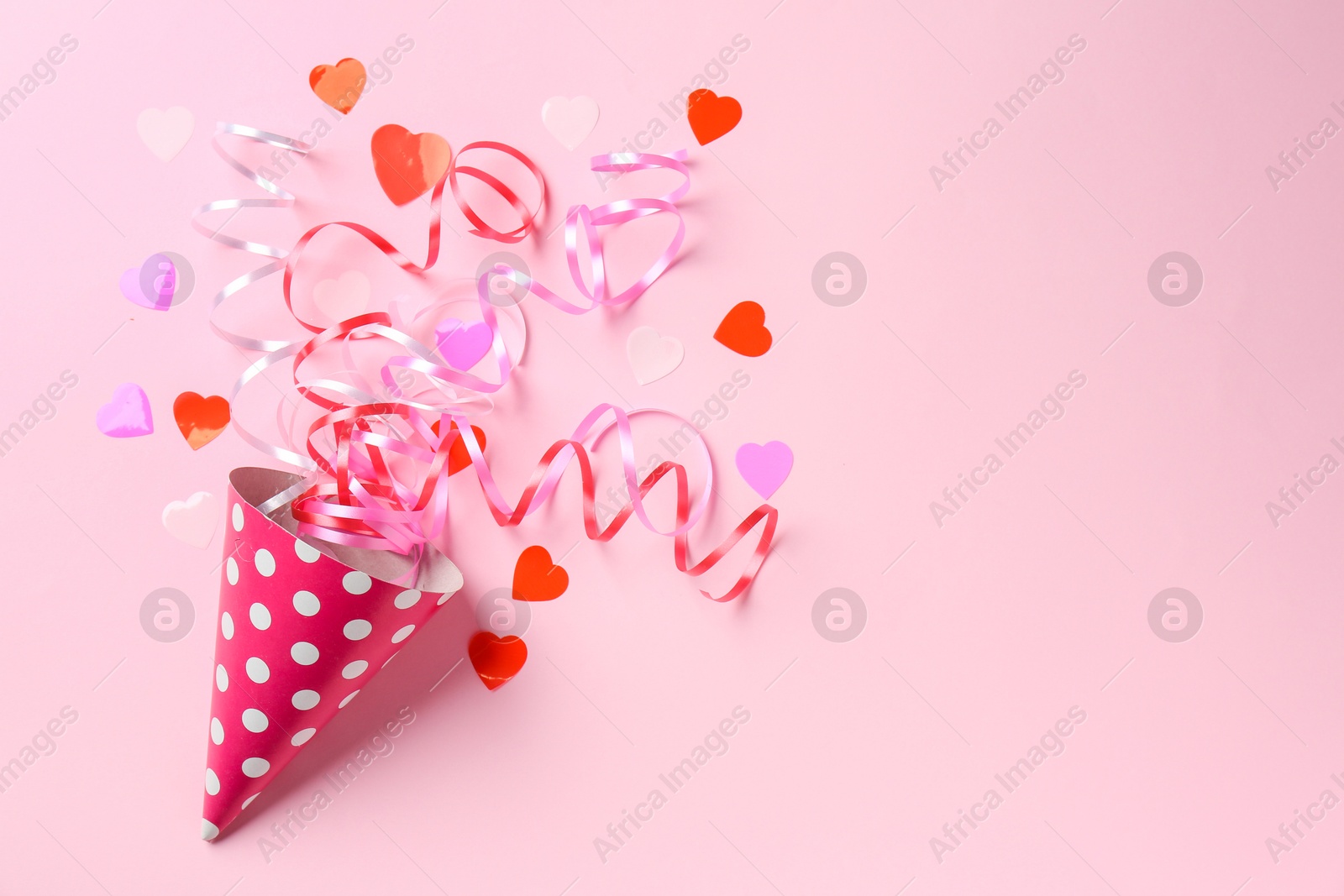 Photo of Party hat with confetti and streamers on pink background, flat lay. Space for text